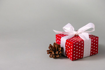 Gift box in red wrapping paper with white polka dots, white bow and pine cone on grey background with copy space