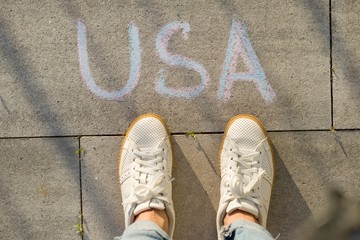 View from above, female feet with text USA written on grey sidewalk
