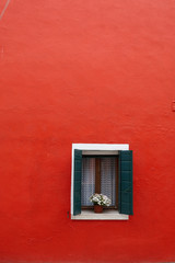 Large red wall with a wooden window with a flower in a pot on the windowsill