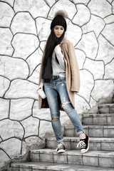 All fashion outfit details. Fashionable woman wearing coat, ripped jeans with sneakers.