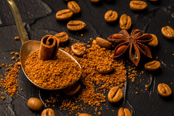 Coffee beans with a vintage spoon of ground coffee and oriental spices, anise and cinnamon. On a dark stone background. Top view. Copy space.