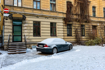 Fototapeta na wymiar At the multi-storey yellow house on the roadside parked snow-covered car.
