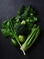 Fresh green food, variety of vegetables, greens and fruits on dark concrete background. Healthy eating concept. Monochromatic idea. Flatlay composition, top view