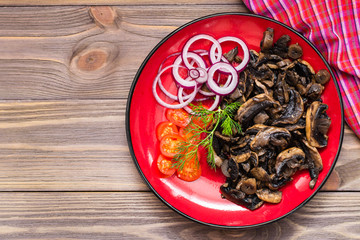 Fried mushrooms, onion and cherry tomatoes on a plate on a wooden table. Top view