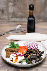 Appetizer of fried mushrooms, onions, tomatoes and poached eggs on a plate on a wooden table