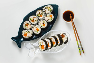 vegan ready-made sushi on the table in fish plates. rolls with fried tofu, cucumber, boiled carrots and fresh avocado. healthy vegan food