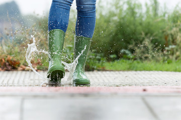Woman in green rubber boots jumping on the puddle water in the street.