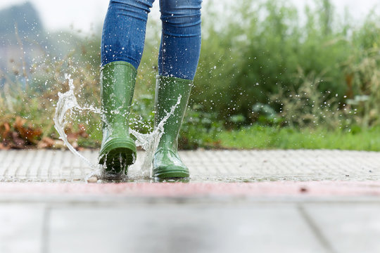 Woman In Green Rubber Boots Jumping On The Puddle Water In The Street.