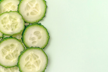 Sliced fresh cucumber on light green background. Close up, top view. With copy space