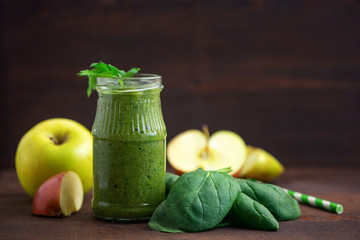 Green spinach smoothies in glass with ingredients on dark wooden table. Side view
