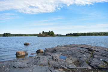 Rocky shore with islands and forest across it under a blue sky