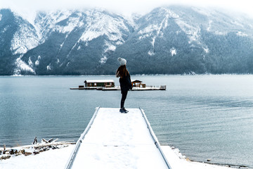 Girl on pier overlooking Lake Minnewanka and snowy mountains in Banff National Park