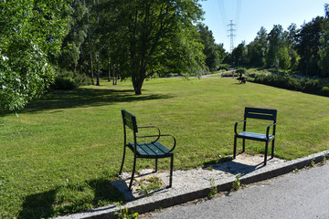 Two empty chairs beside a pathway in a park full of trees and grass