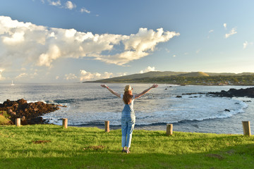 Traveling woman in hat with raised arms near the pacific ocean. Easter island. Chile