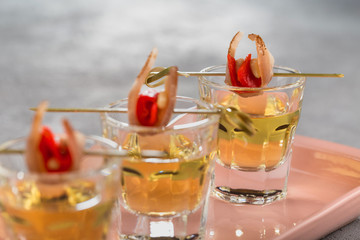 Close-up shot of three glasses of Golden tequila with tapas on skewers with dried meat, baked bell pepper and pine nuts.