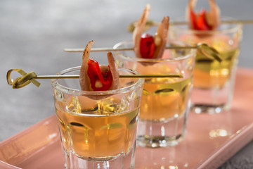 Close-up shot of three glasses of Golden tequila with tapas on skewers with dried meat, baked bell pepper and pine nuts.