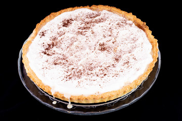 Cream pie with cinnamon on top served in the glass service plate with isolated black background