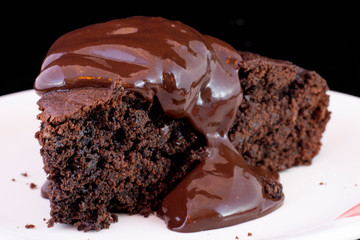 Fresh baked chocolate fudge cake with chocolate dressing on white plate with isolated black background