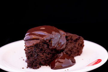 Fresh baked chocolate fudge cake with chocolate dressing on white plate with isolated black background