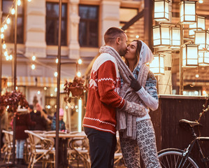 A young romantic couple wearing warm clothes holding hands and kissing standing outdoors at night, enjoying spending time together.