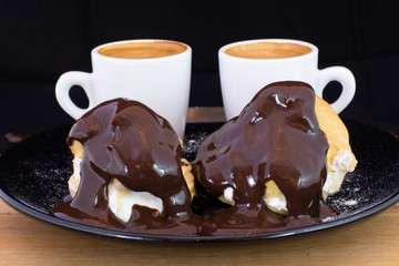 Profiterols and espresso on wood with isolated black background