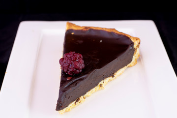 Fresh baked chocolate tart with raspberry on top served on white plate with isolated black background