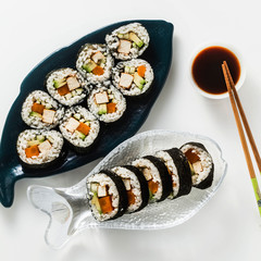 vegan ready-made sushi on the table in fish plates. rolls with fried tofu, cucumber, boiled carrots and fresh avocado. healthy vegan food