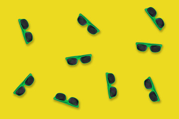 Green sunglasses lying on a yellow like seaside sand background