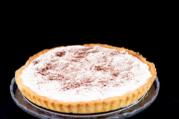 Cream pie with cinnamon on top served in the glass service plate with isolated black background