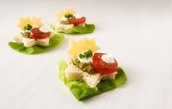 christmas canapes in star shape on lettuce with tomato, pesto and cheese, light background with copy space, close up