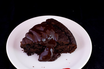 Fresh baked chocolate fudge cake with chocolate dressing on white plate with isolated black background