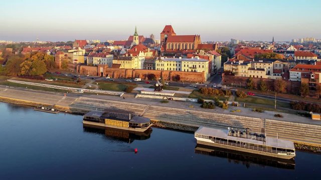 Torun old city in Poland. Aerial approaching 4K video in sunrise light with medieval Gothic St John Cathedral, town hall tower, Vistula river, historic buildings, town walls and gates