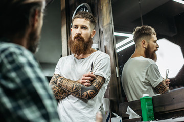 Waist up of thoughtful barber standing with crossed arms and looking