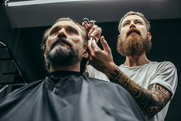 Bottom view of bearded barber working at hairstyle of his client