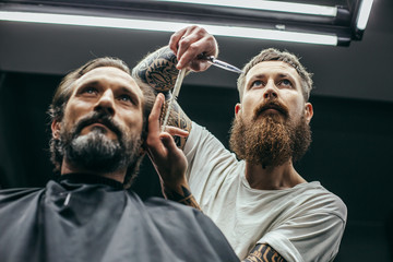 Bottom view of serious barber combing hair of serious man
