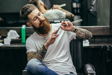 Calm barber touching scissors while sitting alone