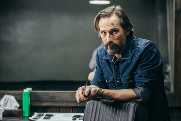 Serious bearded man standing and looking while holding scissors