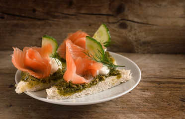 canapes with smoked salmon, cucumber, pesto, cream and dill garnish on a rustic wooden board, copy space, close up
