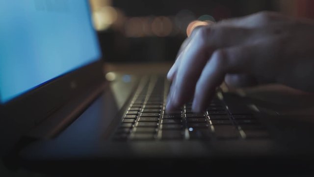 White Man Typing in Laptop Keyboard in Office at Night