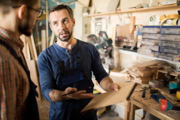 Waist up portrait of two carpenters  discussing project in small woodworking shop, copy space