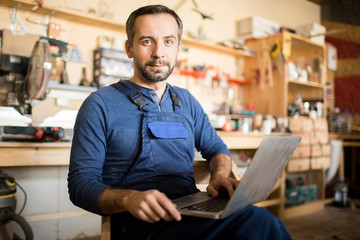 Portrait of mature worker using laptop and looking at camera in workshop interior, copy space