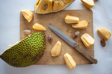 Ripe Jackfruit pieces with jackfruit pods on wooden desk with knife isolated on white