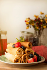 Rolled up crepes, pancakes on a plate with blueberries and strawberries. Vertical image.