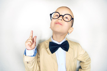Smiling little boy wearing glasses and a bowtie pointing upwards
