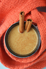 Hot chocolate cup or cocoa drink with cinnamon sticks with orange knitted scarf. Winter background.