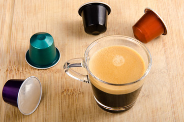 A glass of espresso with nespresso capsules around