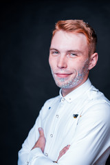 Smiling young man with sparkles beard in white shirt on dark background