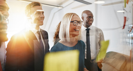 Laughing businesspeople brainstorming with sticky notes on a gla