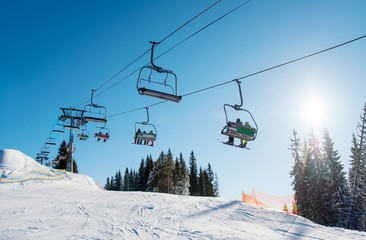 Low angle shot of a ski lift at ski resort Bukovel in the mountains on a sunny winter day. Blue sky, sun and forest on the background copyspace riding top nature extreme sport recreation concept