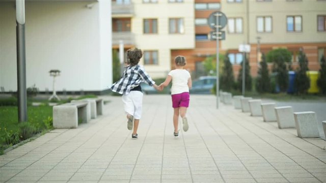 Two Happy Children Run Together Holding Hands. Their Blond Hair Wave Out On The Wind.